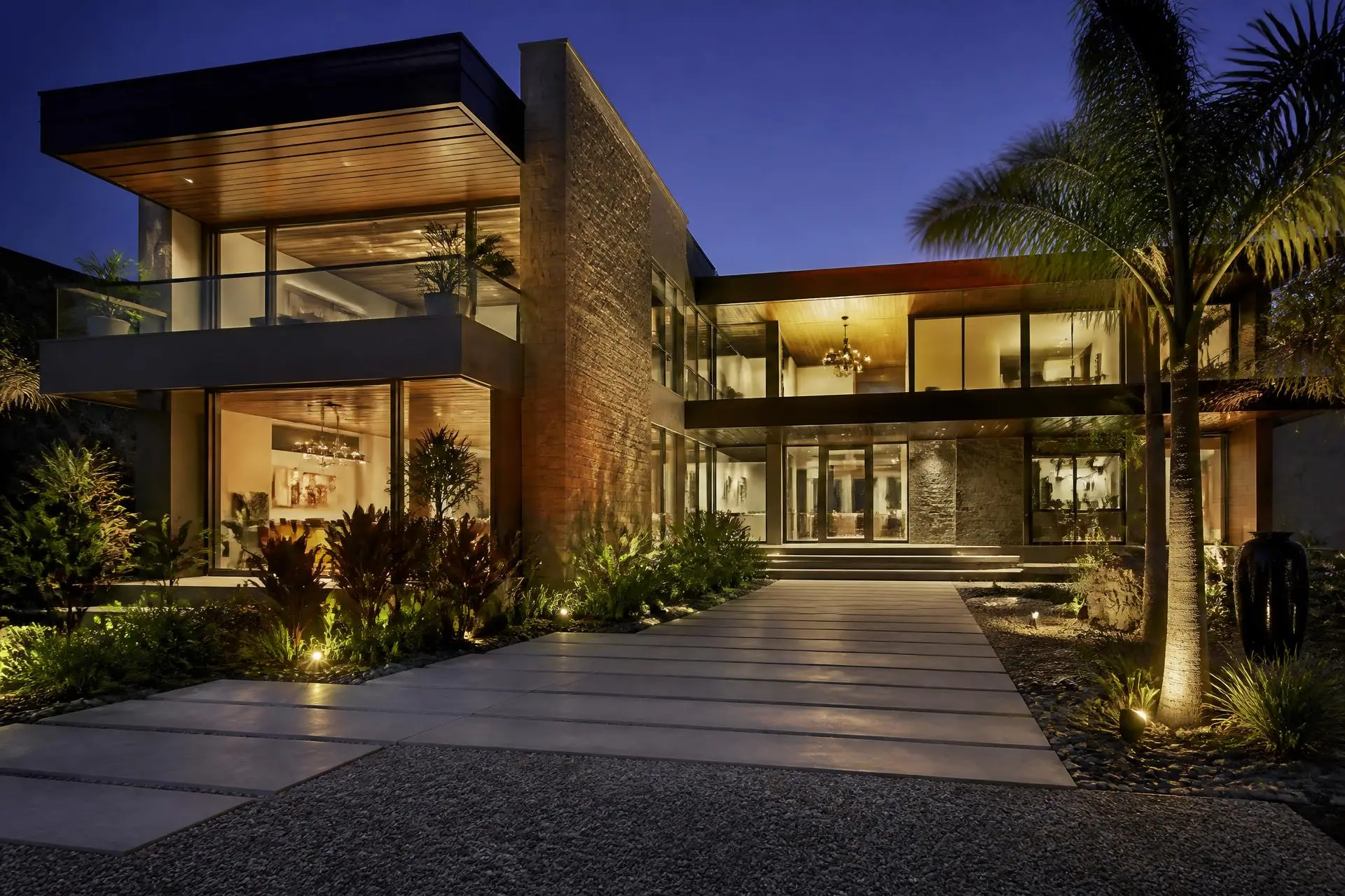 Fachada de residência contemporânea de alto padrão ao entardecer, com vidro, madeira e pedra
